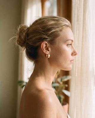 Chunky Huggie Hoops – gold-tone chunky huggie hoop worn on a model by a window, side profile