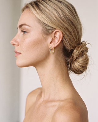 Model wearing a gold-tone Crystal Huggie hoop earring, hair in a low bun