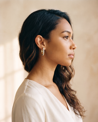Model wearing a gold-tone Crystal Huggie hoop earring, side profile