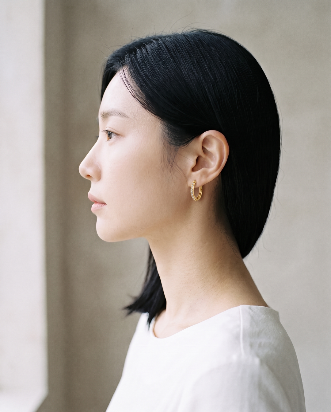 Model wearing a gold-tone Crystal Huggie hoop earring, dark hair tucked back