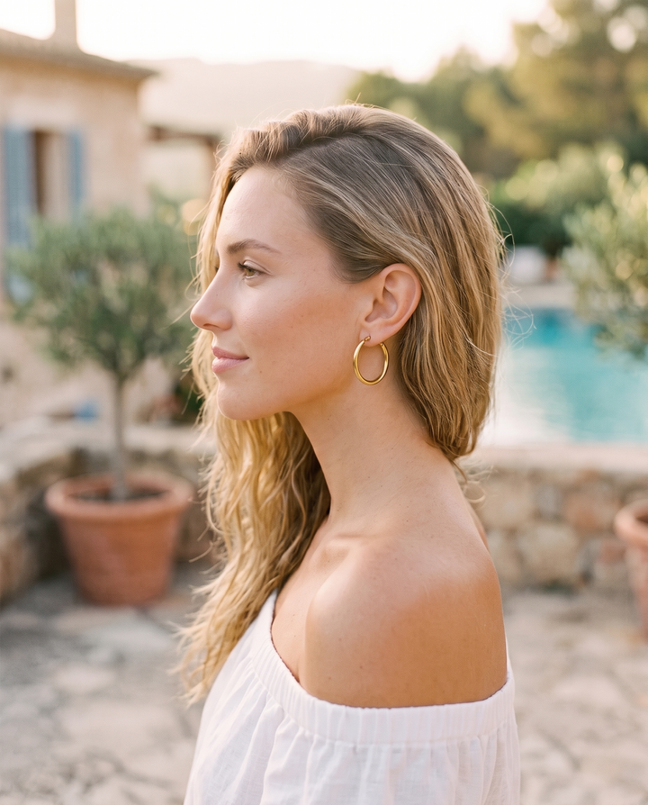 Everyday Hoops: model wearing a thin gold-tone hoop earring outdoors, side profile
