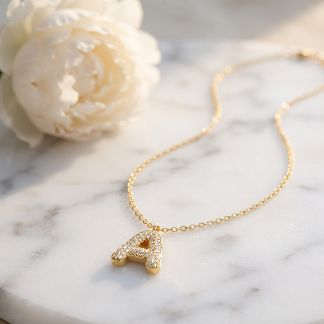Bubble Initial Crystal Necklace on marble with a peony