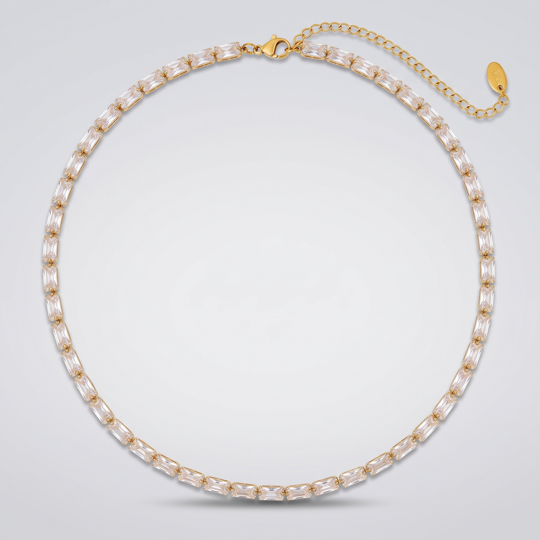 Classic Tennis Necklace in gold-tone with clear baguette zirconia stones, laid flat on a grey background