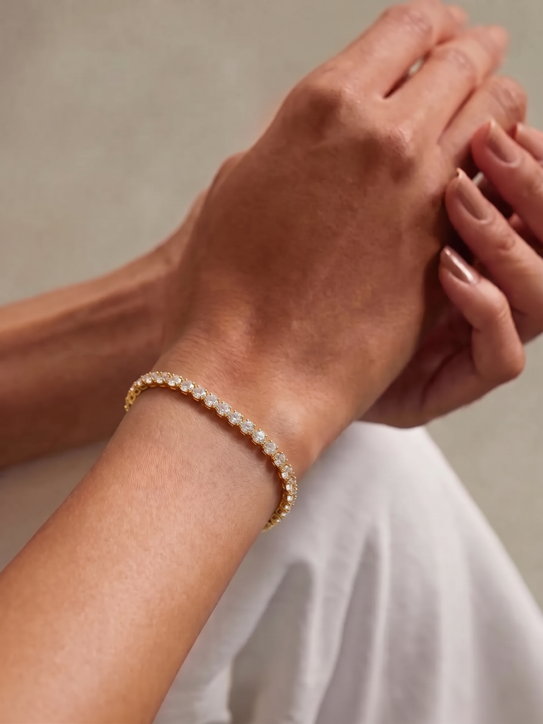 Petite Tennis Bracelet worn on the wrist, two hands crossed over white fabric