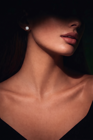 Model wearing a Classic Solitaire Stud in gold-tone, face half in shadow