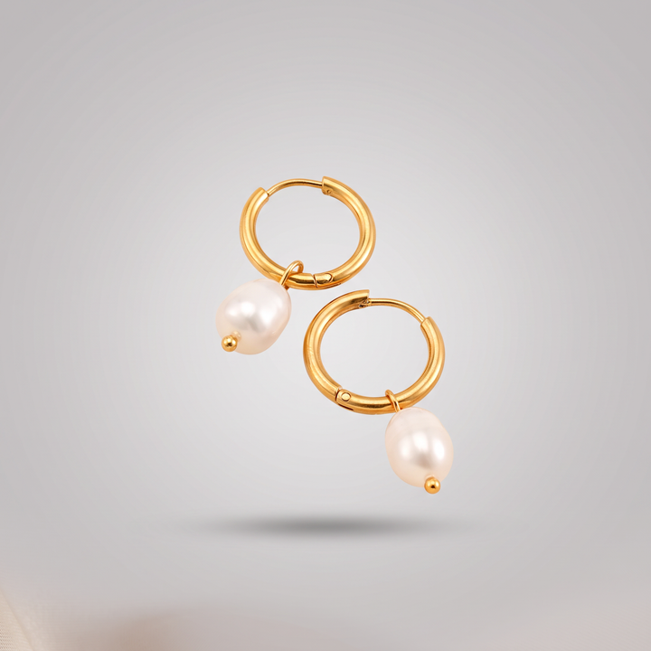 Pearl Drop Huggies in gold: pair of small gold-tone huggie hoops, each with a white freshwater pearl drop, front view on grey