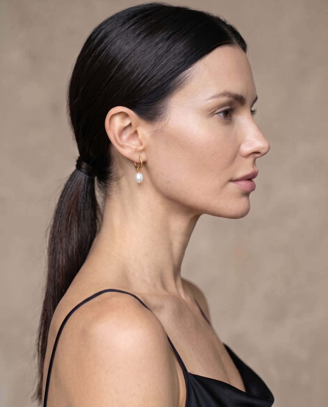 Pearl Drop Huggies in gold worn on the ear, side profile, pearl hanging just below the lobe