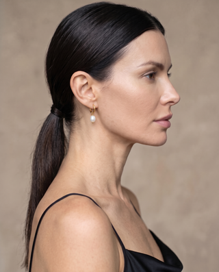 Pearl Drop Huggies in gold worn on the ear, side profile, pearl hanging just below the lobe