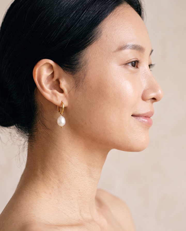 Pearl Drop Huggies in gold worn on the ear, close-up of the huggie hoop and pearl drop