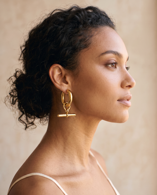 Model with curly hair wearing a gold-tone T-Bar Hoop earring, side profile